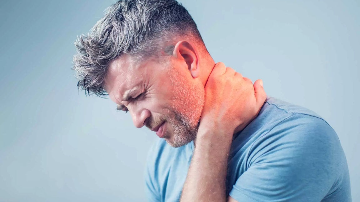 Hombre de pelo gris y barba corta, vestido con una camiseta azul y llevándose la mano al cuello con expresión de dolor. La zona del cuello está resaltada en rojo para indicar dolor de cuello.