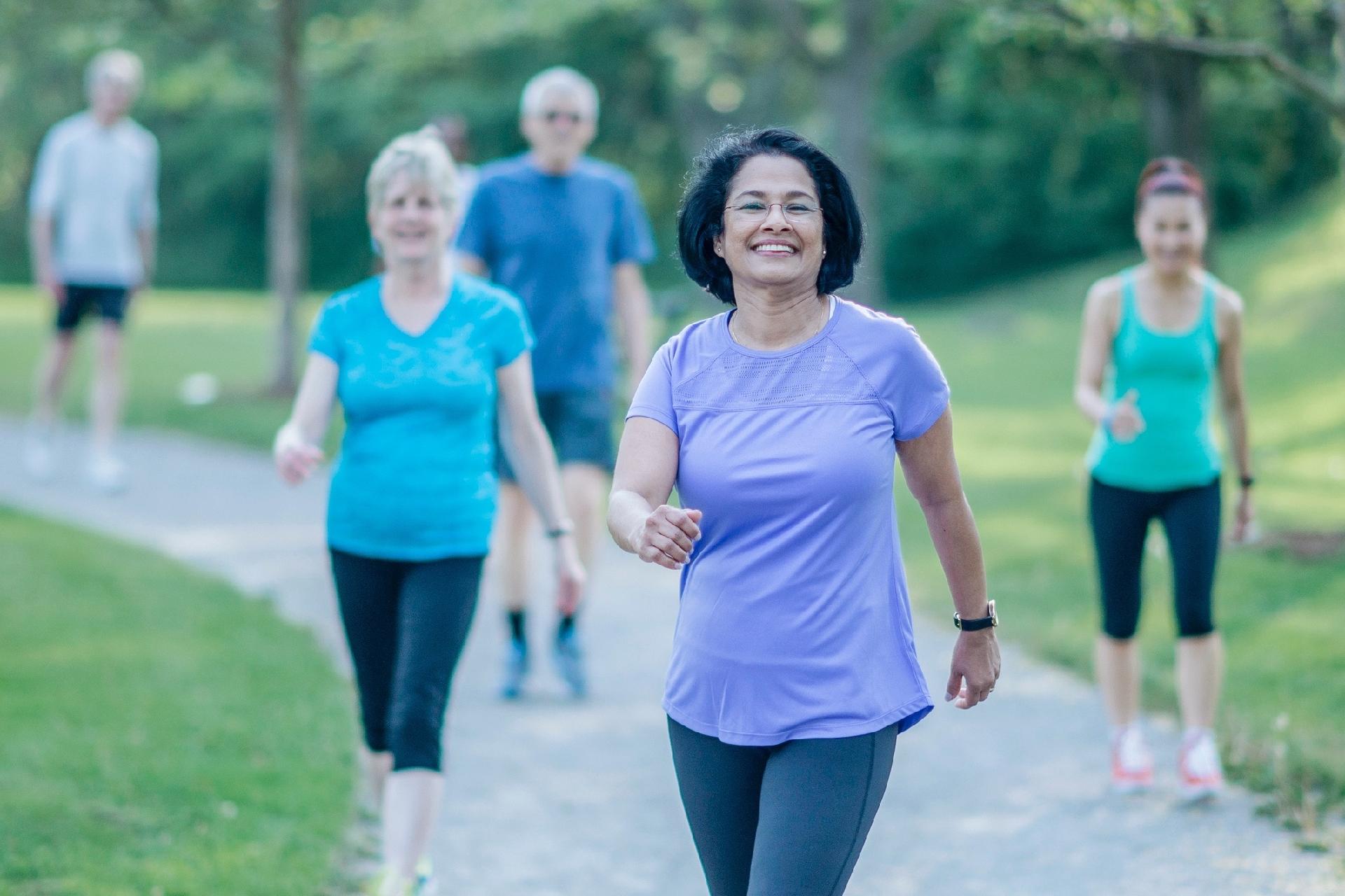 Un grupo de adultos camina al aire libre en un parque, con ropa deportiva. 