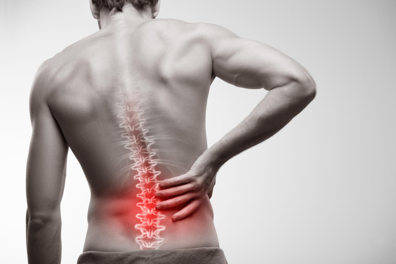 Hombre sujetándose la parte baja de la espalda con la mano, lo que pone de manifiesto el dolor lumbar. La imagen muestra una columna vertebral superpuesta, con una zona roja que indica el punto de mayor dolor e inflamación.